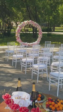 beautiful wedding venue with flower garland and chairs near table with treats in green park on autumn day upper view