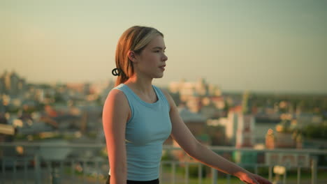 side view of lady roller skating near iron railing under warm evening sunlight, gently swinging her hands as she moves, with blurred cityscape and buildings in background