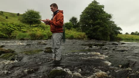 slow panning shot of a fly fisherman wading and casting his line into the river