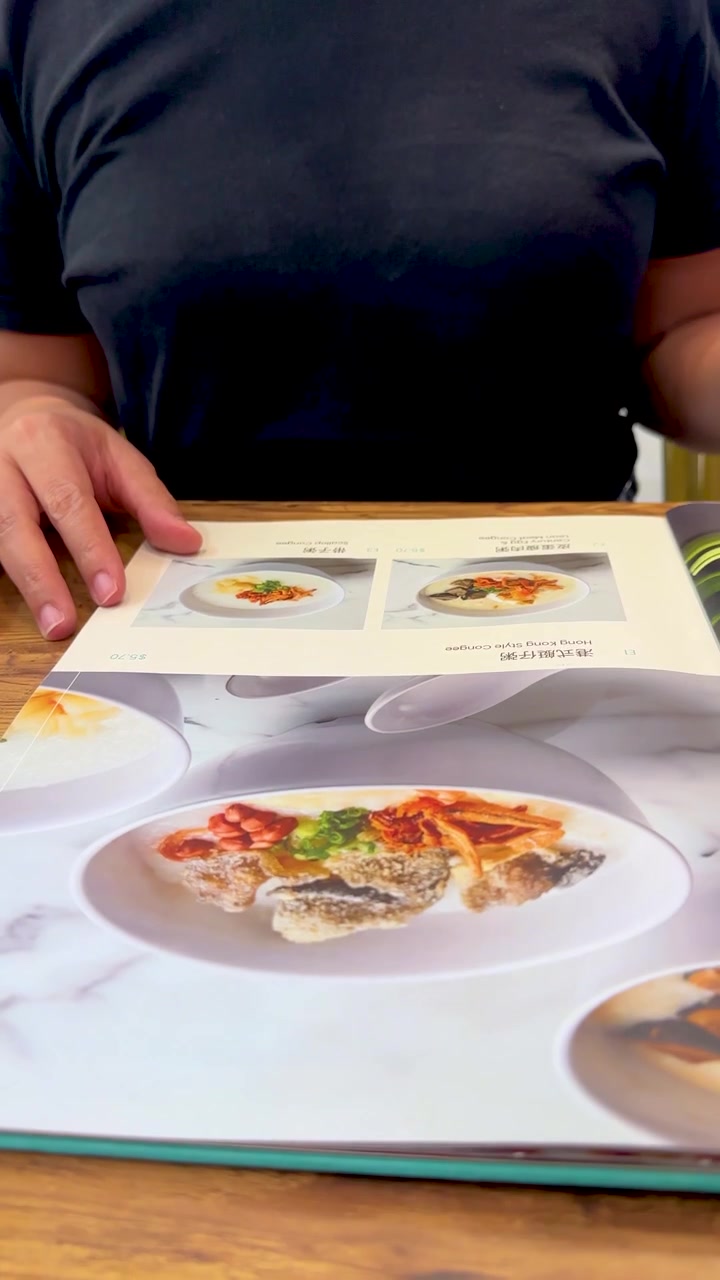 En person bladrer i siderne af en illustreret madmenu i lyse, afslappede restaurantomgivelser med naturligt lys.
