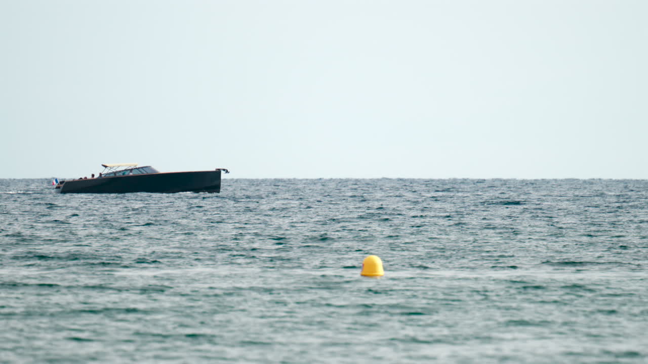 Stylish dark hulled speedboat gliding across the open sea with sailboats on the horizon