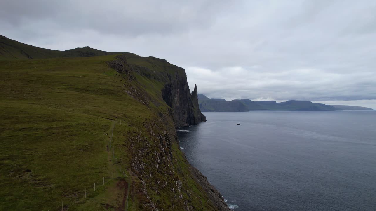 disparo de avión no tripulado ascendente de una mujer observando la hermosa costa y la pila de mar de trollkonufingur en sandavagur en la isla de vagar durante un día nublado