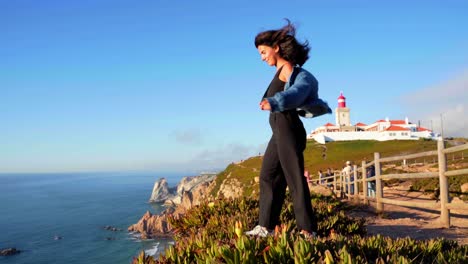 a girl stands on the edge of a cliff enjoying the view at the lighthouse at cabo da roca in sintra, portugal