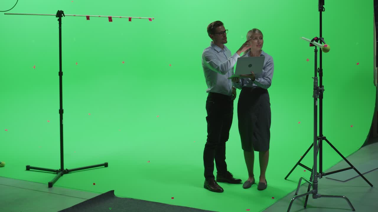 평범한 옷을 입은 여성과 남성 동료가 녹색 화면으로 노트북 컴퓨터를 사용하여 이야기하고 크로마 키 스튜디오를 모방합니다. 비즈니스, 기업 사무실, 작업, 기술 개념.