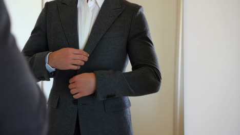 man adjusting his suit jacket in front of a mirror