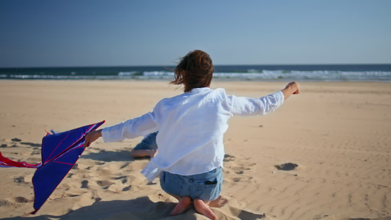 Mother son having fun together flying kite on summer beach. Active boy playing