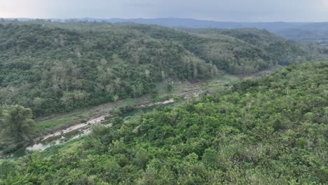 Drone-Pasando-A-Lo-Largo-De-Secciones-Del-Río-Oyo-Adyacentes-Al-Puente-Gantung-Wanagama-Cerca-De-Desa-Wisata-Jekok-Al-Comienzo-De-La-Estación-Seca---Con-Follaje-A-Juego