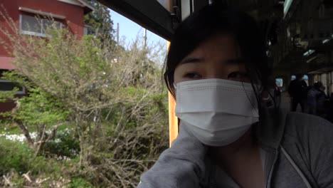 young japanese girl wearing facemask against corona looking out of moving train