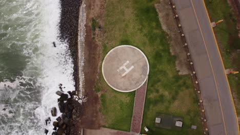 helipad by the beach shore, near a coastal freeway and with waves braking to its left