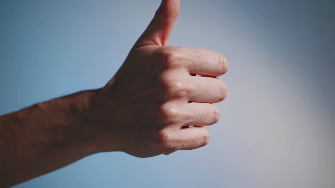 Close-up video of a hand giving a thumbs-up against a blue background