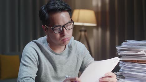 집에서 문서와 함께 열심히 일하면서 머리를 흔들고 있는 피곤한 아시아인