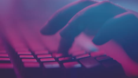 persona escribiendo en un teclado en la oscuridad con iluminación de colores.