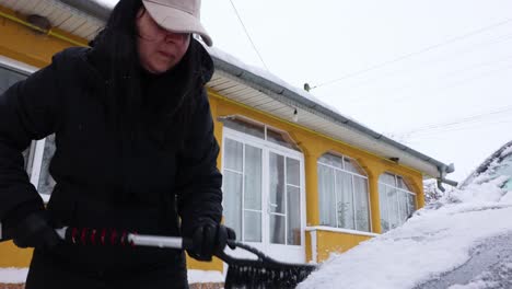 woman cleaning car from snow in winter season - close up