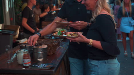 people serving and eating food at an outdoor market stall