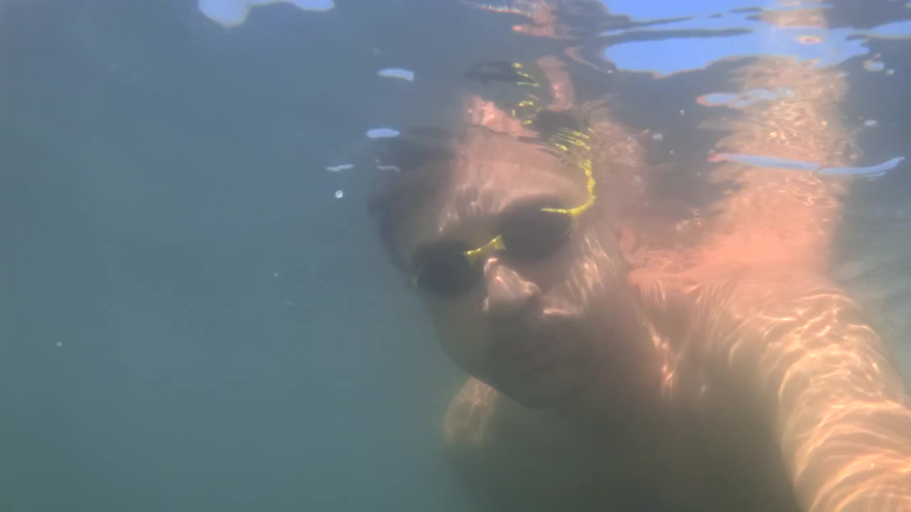Man with goggles taking a selfie while swimming underwater, enjoying a summer leisure activity. Clear blue water above