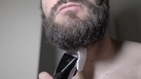 close up: man trimming thick beard with electric groomer