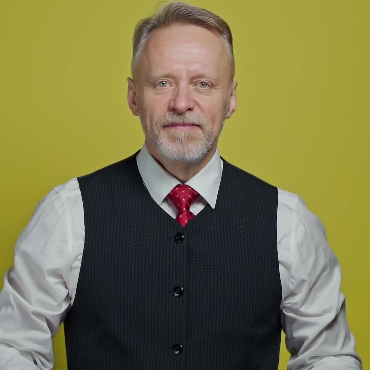 Portrait of a handsome grey-haired man. Mature man taking off his eyeglasses with a smile and looking at camera on yellow background.