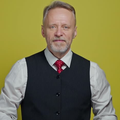 portrait of a handsome grey-haired man. mature man taking off his eyeglasses with a smile and looking at camera on yellow background.