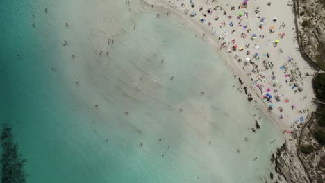 Toma-Aérea-De-Arriba-Hacia-Abajo-De-La-Pelosa,-Una-De-Las-Playas-Más-Hermosas-De-Cerdeña,-Rodeada-Por-Aguas-Cristalinas-De-Color-Esmeralda-Y-Arrecifes