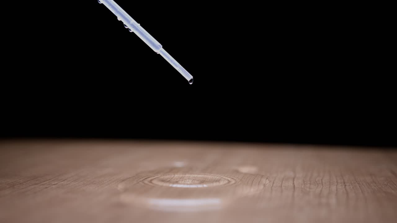 Droplet of water suspended in air falling from a pipette, creating a ripple effect on wood