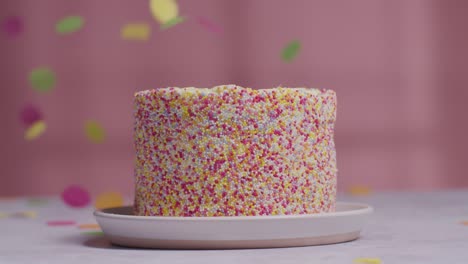 studio shot of paper confetti falling on birthday cake covered with hundreds and thousands decorations 2