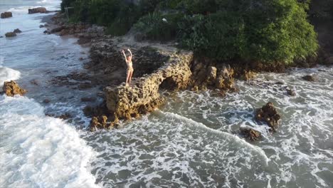 Niña-De-Pie-Sobre-Una-Roca-En-El-Borde-Del-Océano-De-Brasil-Durante-La-Puesta-De-Sol