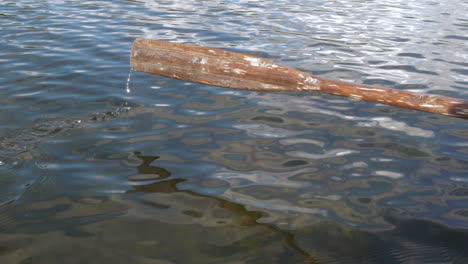 wooden oar sweeping into rippling water on lake, slow motion shot