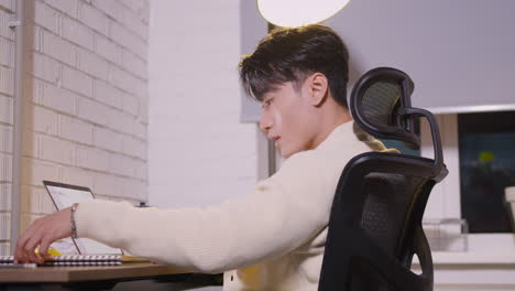 side view of an male employee typing on laptop computer and writing something in notebook at the office