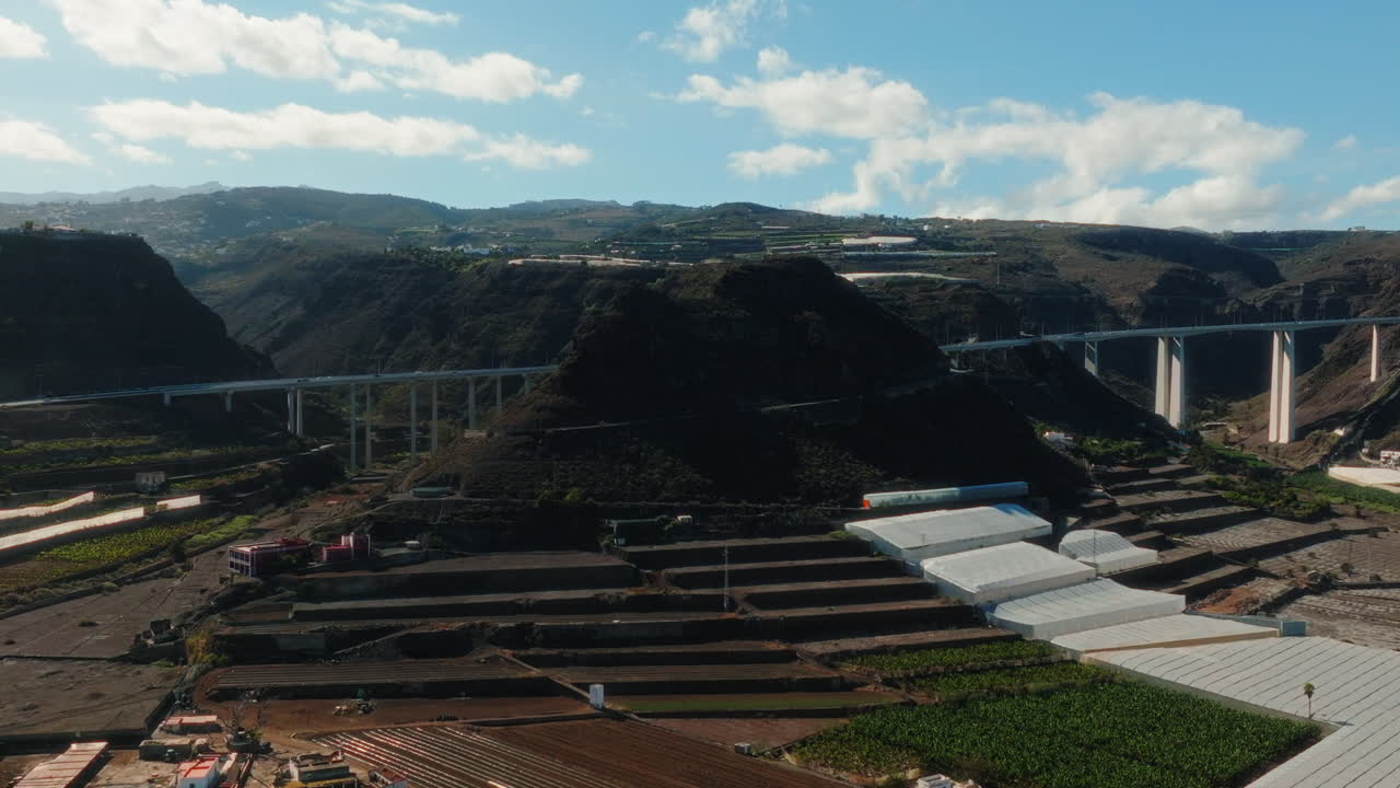Aerial: white bridge in a valley with traffic and a hill during the day in Gran Canaria, Spain, orbit drone shot