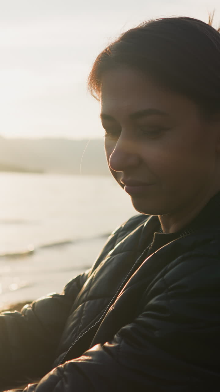 una mujer molesta se sienta junto al lago recordando el pasado al atardecer. una joven con rostro triste trata de hacer frente a las emociones negativas debido al divorcio. se enfrenta a desafíos emocionales sola