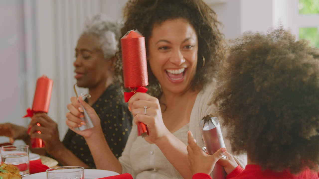 Familia multigeneracional sentada alrededor de la mesa en casa tirando de los crackers antes de comer la cena de Navidad