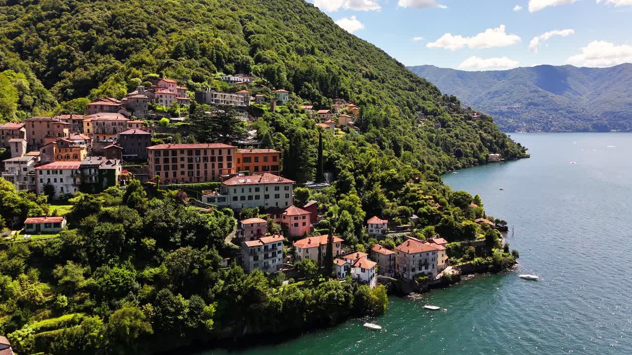 Scenic view of Nesso on Lago di Como, Italy, featuring hillside homes surrounded by dense greenery above calm blue water, with mountain slopes forming a peaceful lakeside setting under warm skies