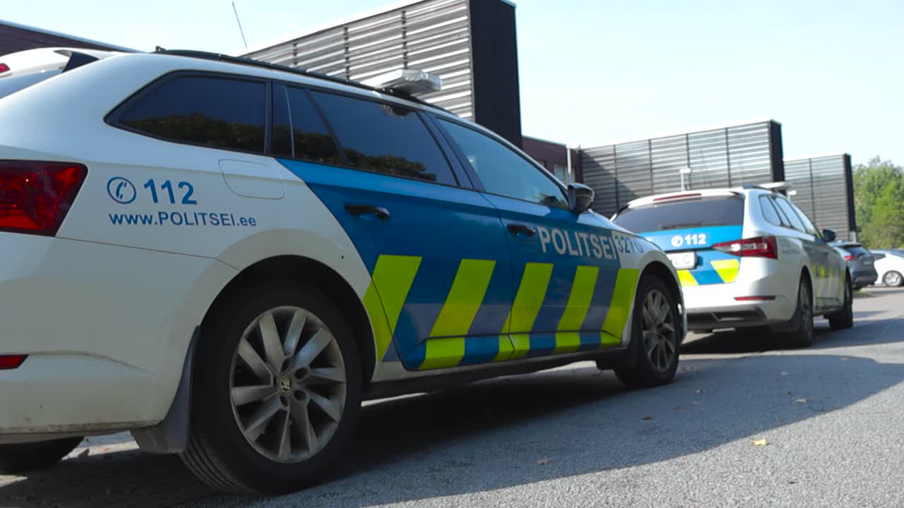 Two Estonian police vehicles or cars parked outside of an apartment building while officers are on duty during a summer or autumn sunshiny day. Parked at Laagri Tallinn on asphalt, blue and white.