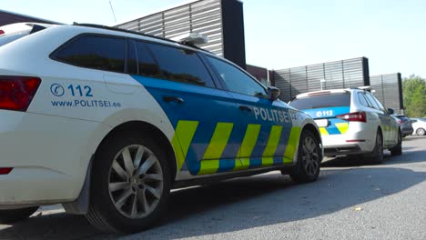 two estonian police vehicles or cars parked outside of an apartment building while officers are on duty during a summer or autumn sunshiny day. parked at laagri tallinn on asphalt, blue and white.
