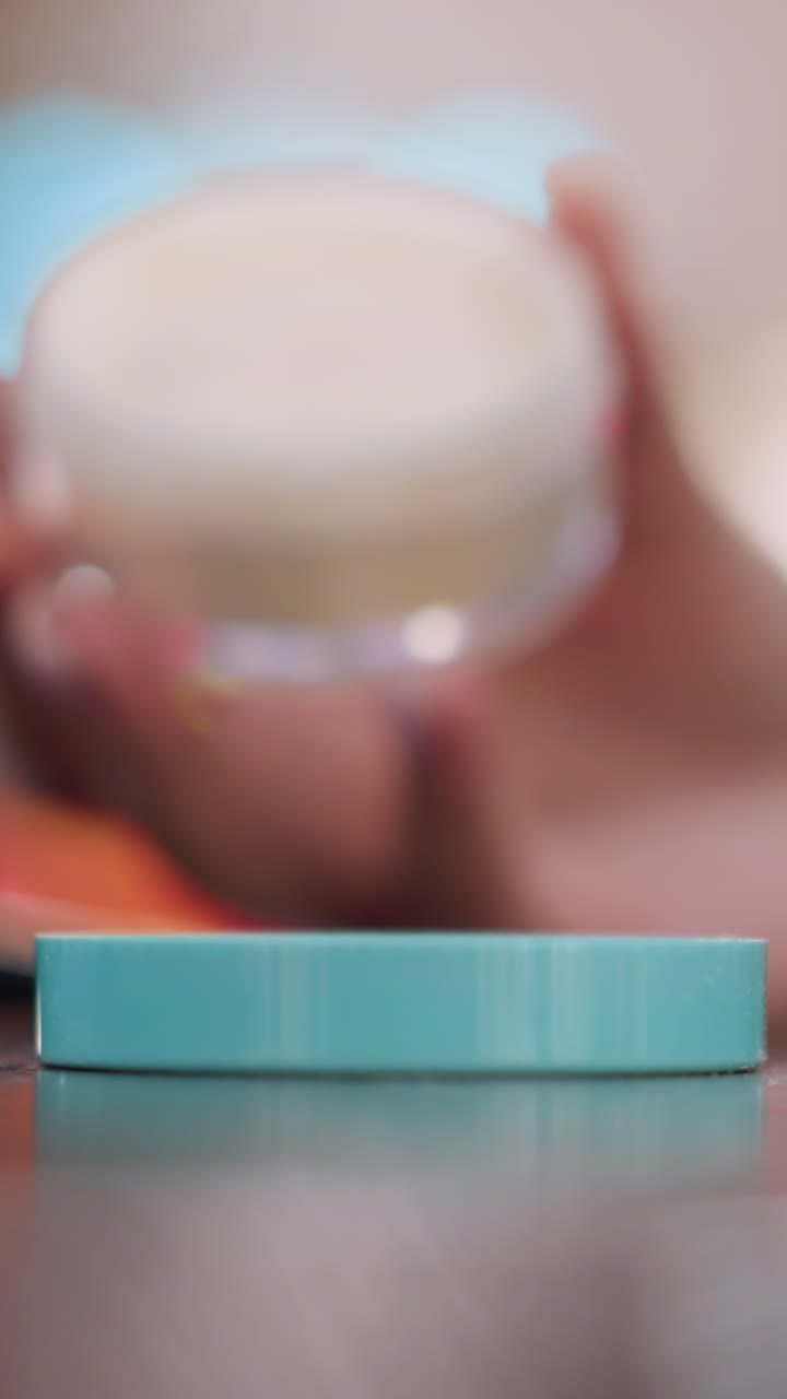 Primer plano de tapa turquesa y frasco de cosméticos, creador de contenido de belleza que sostiene suavemente un envase de polvos sueltos sobre la tapa, uñas cuidadas, luces bokeh suaves, iluminación cálida de estudio, detalles de textura refinados para el producto