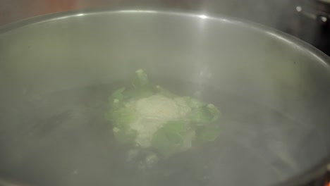 whole head of cauliflower boiling in large metal pot, close up