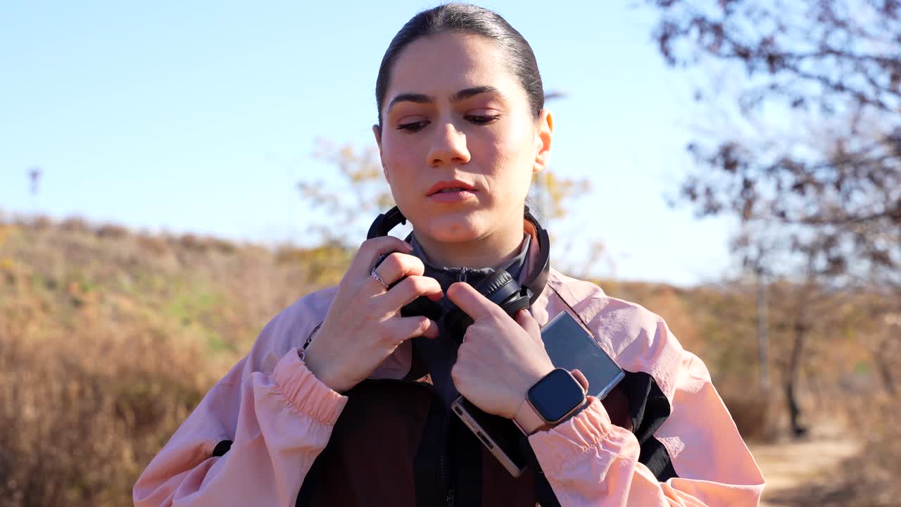 joven atlética eligiendo una canción con el teléfono y poniendo sus auriculares antes de una carrera en el parque