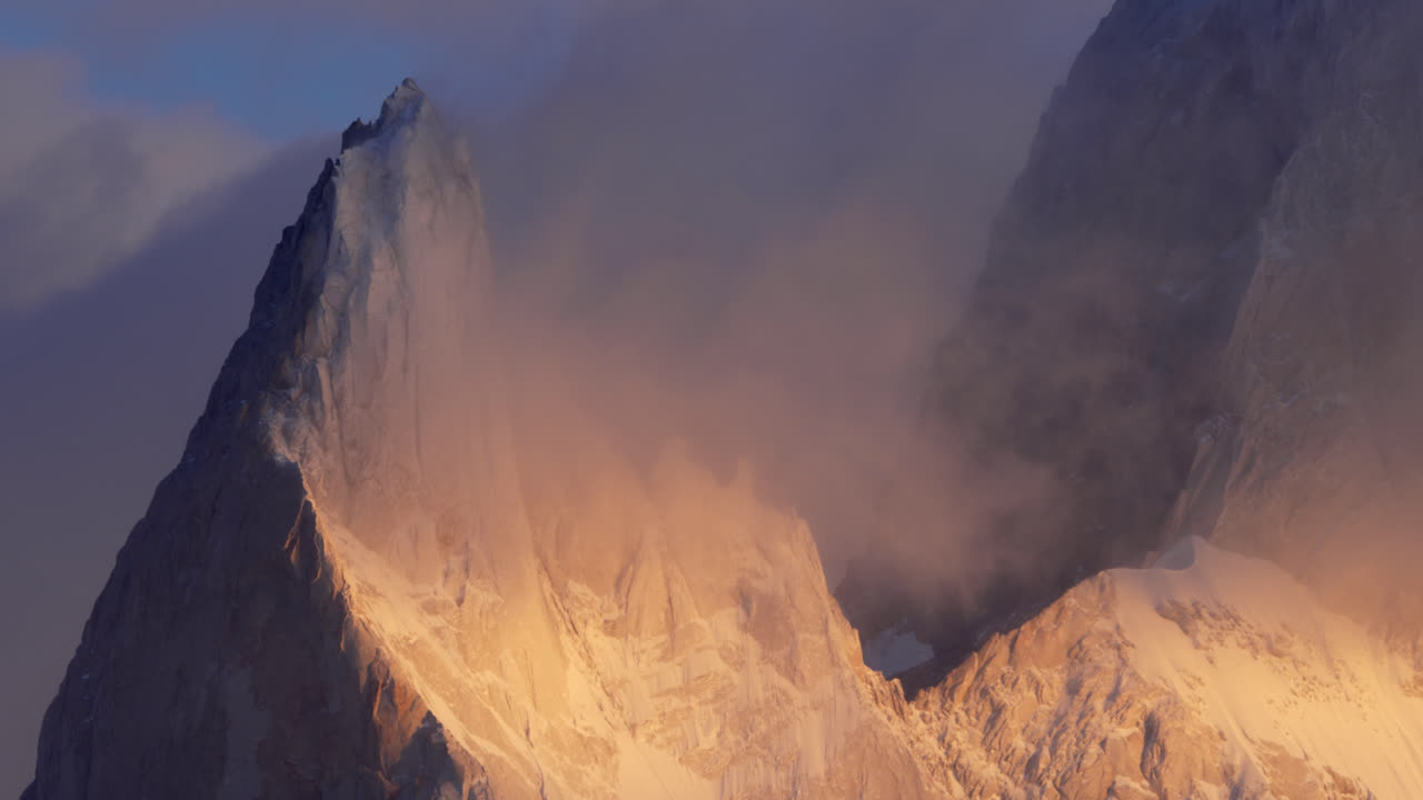 Dramatic shot of Mount Fitz Roy at sunrise, with clouds enveloping the peak, soft light