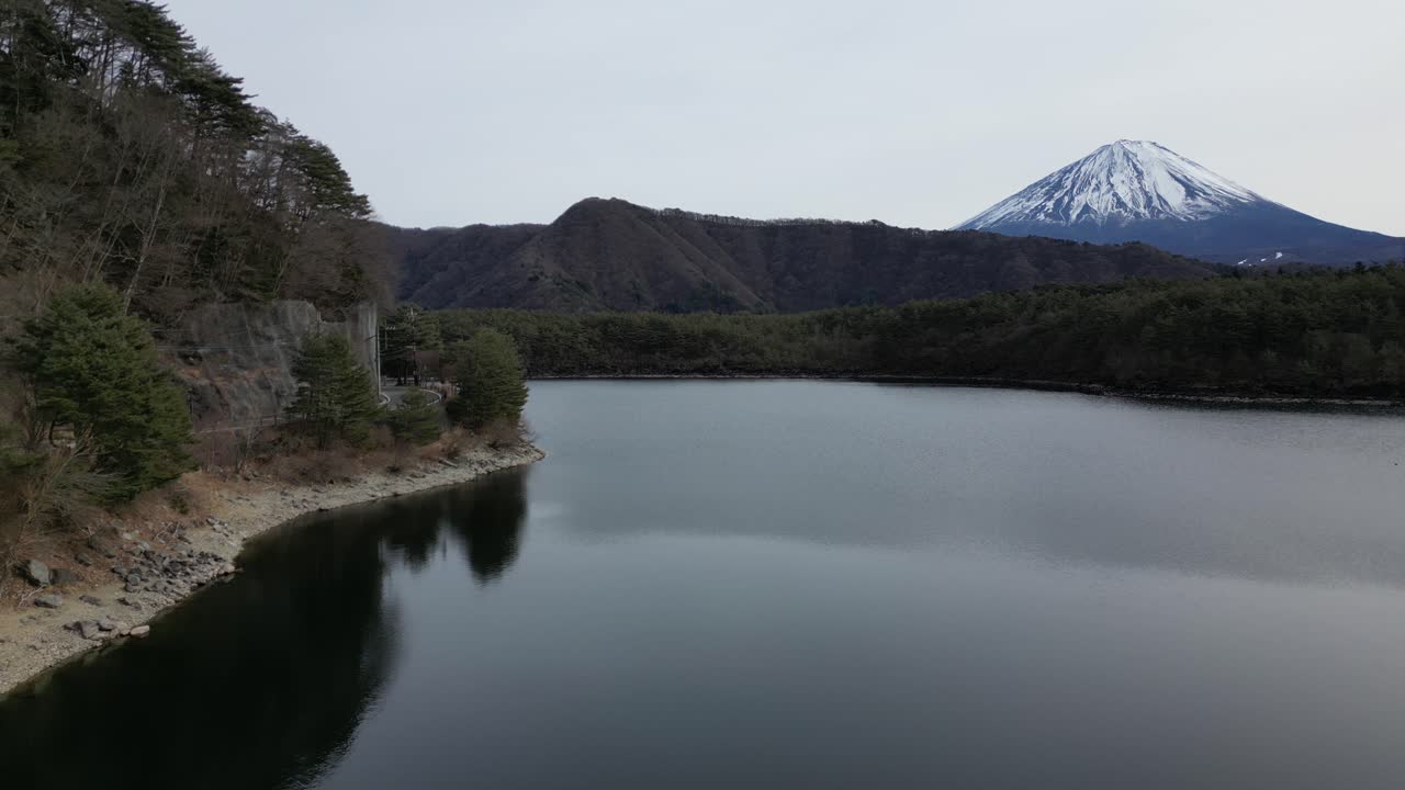 Scorcio suggestivo del Monte Fuji con lago calmo e una strada visibile sul lato sinistro. Paesaggio giapponese sereno che unisce il viaggio nella natura e una tranquilla presenza umana.