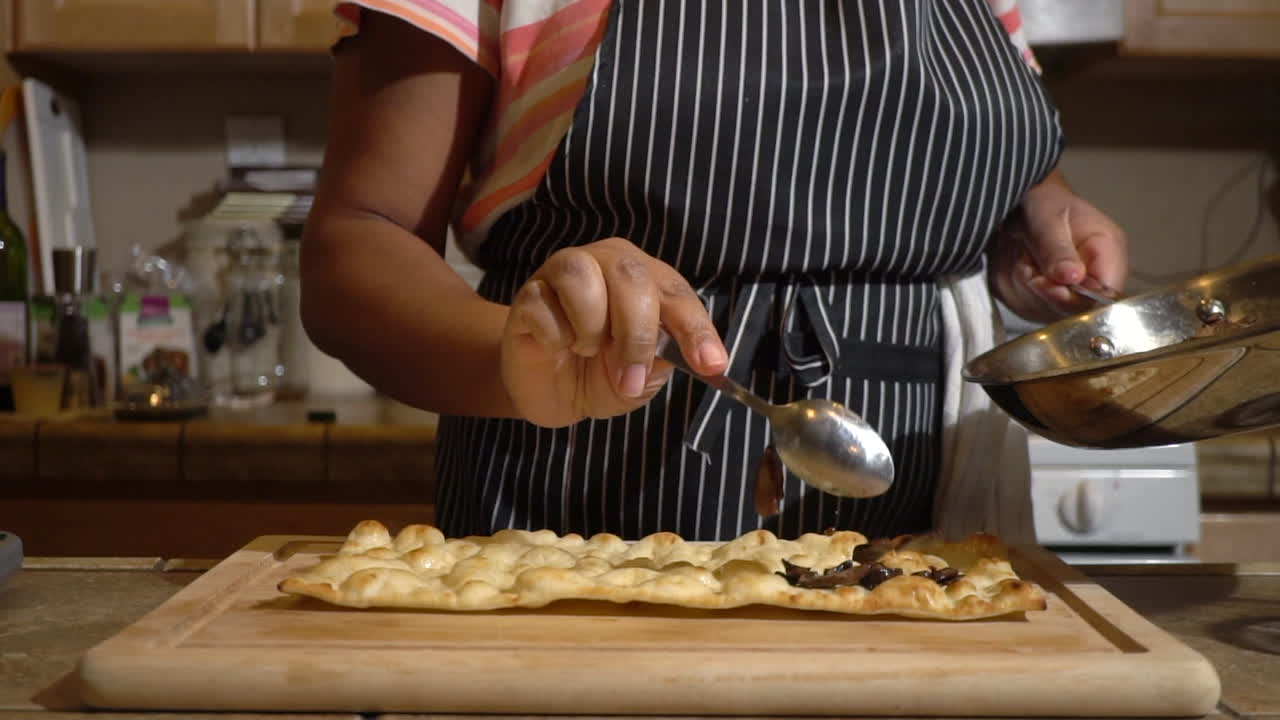 Female cook pours hot fried mushroom slices on flatbread, slow motion