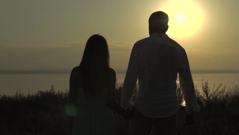 couple walking hand-in-hand at sunrise over lake