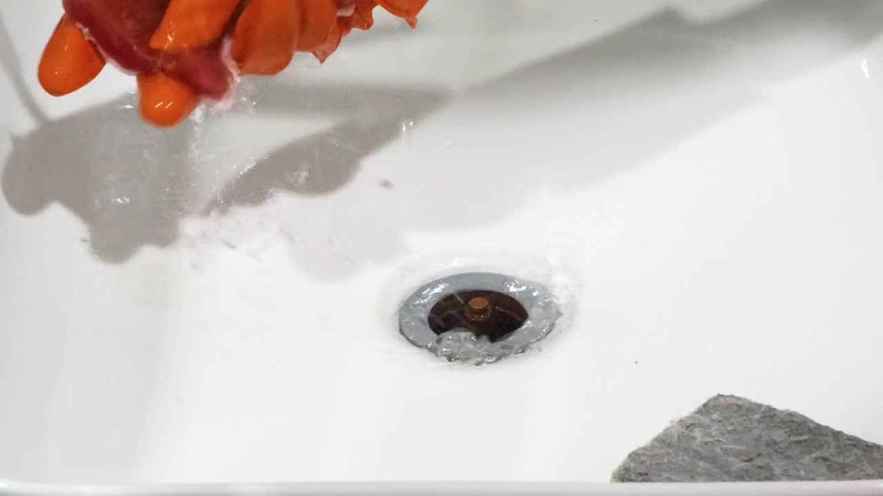 Washing an object in a sink with orange gloves