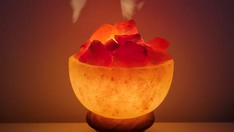 Himalaya-Salzlampe,-Die-Auf-Einem-Tisch-Vor-Dunklem-Hintergrund-Leuchtet,-Rotiert,-Nahaufnahme