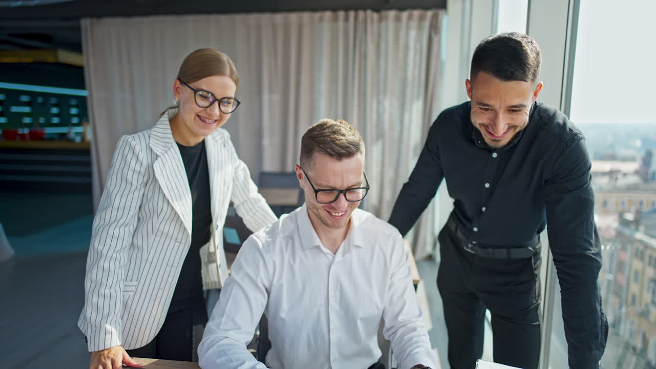 Company employees standing over the male office worker. Three people looking at computer screen with interest, discussing and smiling.