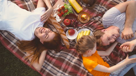 top view of happy family lying on blanket in park, laughing and having fun together while having a picnic in the park 1