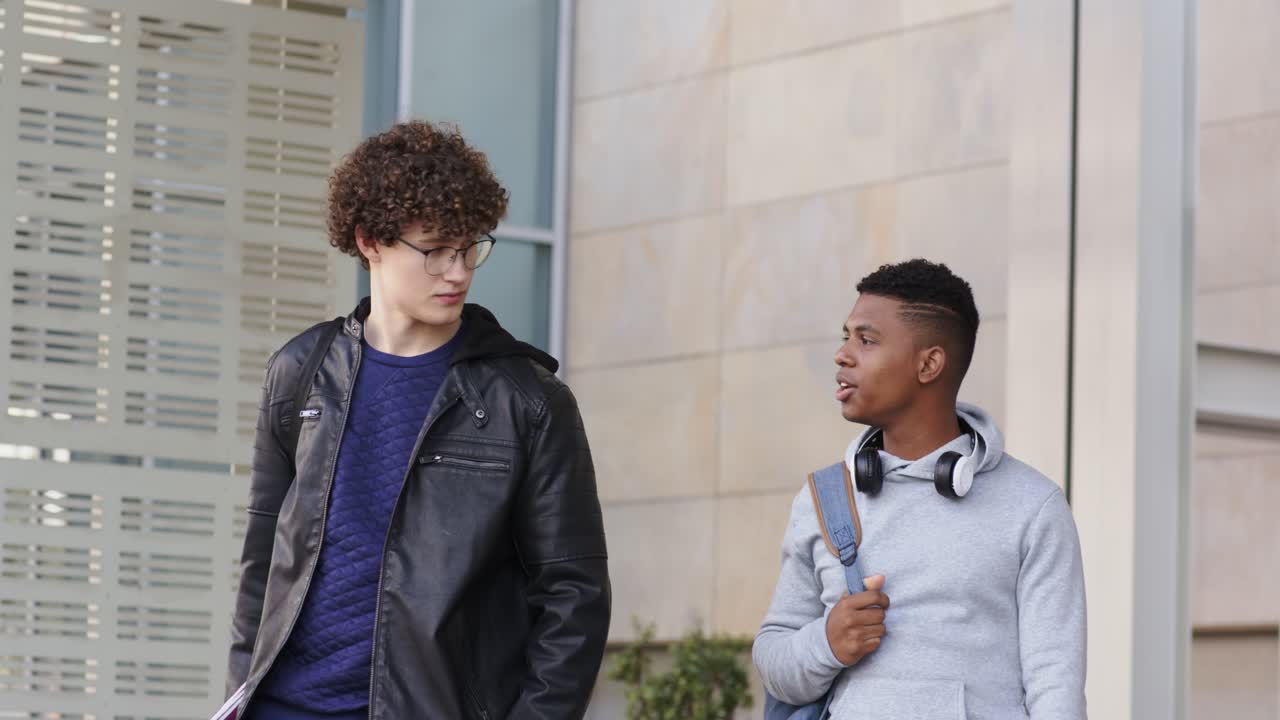 Dois amigos do sexo masculino caminhando pela fachada com um pacote, o companheiro apontando para si mesmo enquanto o líder escuta