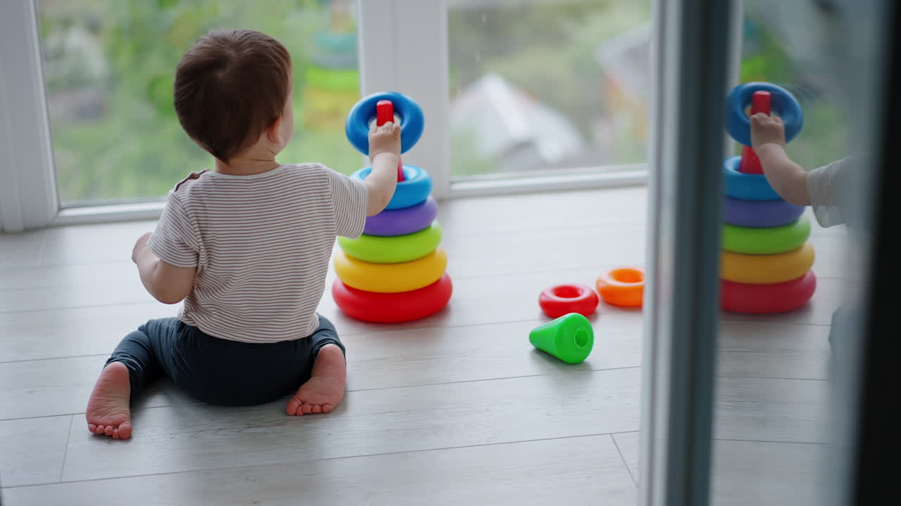 Rear view of Caucasian toddler playing with pyramid. Peaceful child assembling a pyramid on a balcony.