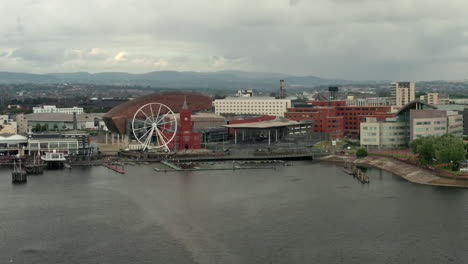 narrow aerial flyover of cardiff bay pulling back from the quayside on a cloudy summer’s day with passenger ferry - sailboat in foreground