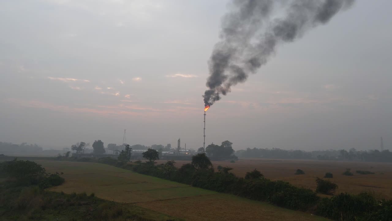 volando verso una raffineria di petrolio con un camino in fiamme e fumo nero che inquina i terreni agricoli circostanti in bangladesh