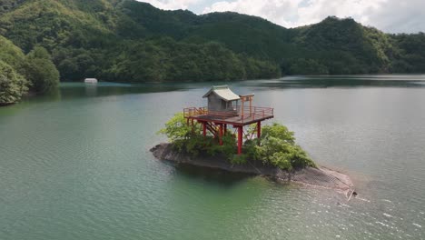 Aerial-Drone-fly-Shinto-Shrine-Japanese-Temple,-Middle-of-Water-Wide-River-Tori-orange-entrance,-along-green-and-blue-island-summer-Japan-landscape-in-Kyoto-Prefecture